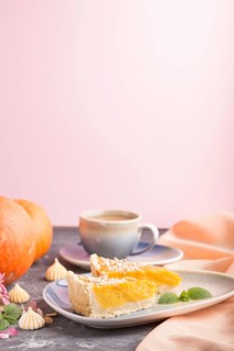 Two pieces of traditional american pumpkin pie with cup of coffee on a black and pink background
