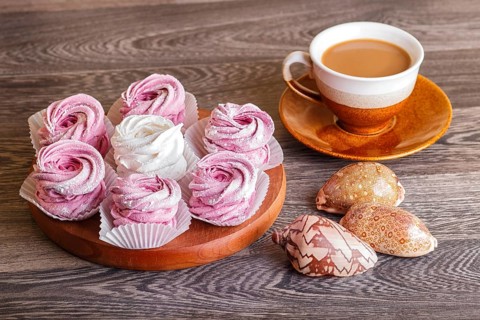 Pink and white homemade marshmallows (zephyr) on a round wooden board with cup of coffee and