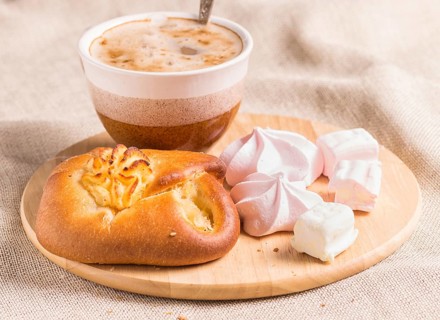 Sweet buns, meringues and coffee cup on a wooden board and linen tablecloth