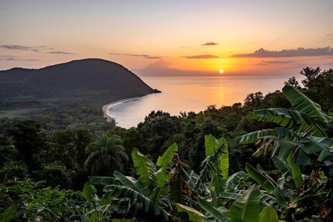 View from a mountain to a secluded bay with a sandy beach and mangrove forest. The sun rises over