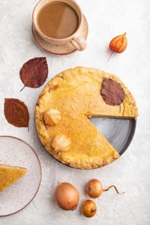 Autumn onion pie decorated with leaves and cup of coffee on gray concrete background. Top view,
