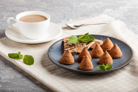Chocolate truffle on blue ceramic plate and a cup of coffee on gray concrete background. close up,