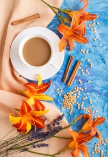 Orange day-lily and lavender flowers and a cup of coffee on a blue concrete background, with orange