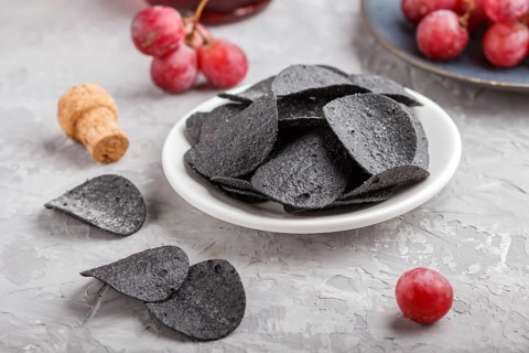 Black potato chips with charcoal, balsamic vinegar in glass, red grapes on a blue ceramic plate on