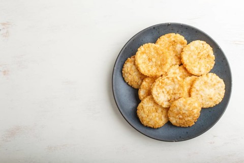 Traditional japanese rice chips cookies with honey and soy sauce on a blue ceramic plate on a white