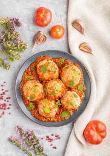 Pork meatballs with tomato sauce, oregano leaves, spices and herbs on blue ceramic plate on a gray