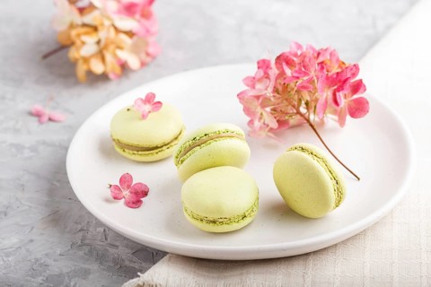 Green macarons or macaroons cakes on white ceramic plate on a gray concrete background and linen