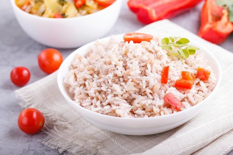Unpolished rice porridge with stewed vegetables and oregano in white bowl on a gray concrete