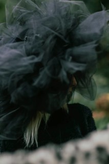 Side view of a woman in a large tulle hat, partially obscured by a blurred foreground