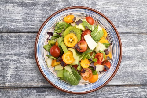 Vegetarian salad of pac choi cabbage, kiwi, tomatoes, kumquat, microgreen sprouts on gray wooden