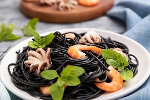 Black cuttlefish ink pasta with shrimps or prawns and small octopuses on gray wooden background and