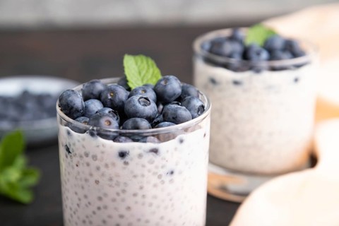 Yogurt with blueberry and chia in glass on black concrete background and orange linen textile. Side