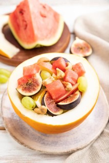 Vegetarian fruit salad of watermelon, grapes, figs, pear, orange, cashew on white wooden background
