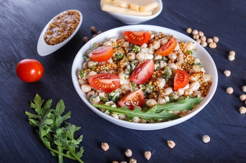 Vegetarian salad of boiled chickpeas, cheese, arugula, mustard and cherry tomatoes on black wooden