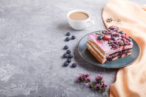 Berry cake with milk cream and blueberry jam on blue ceramic plate with cup of coffee and fresh
