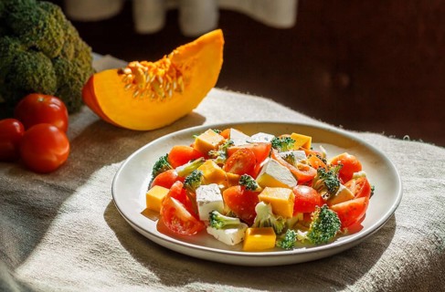 Vegetarian salad with broccoli, tomatoes, feta cheese, and pumpkin on white ceramic plate on linen