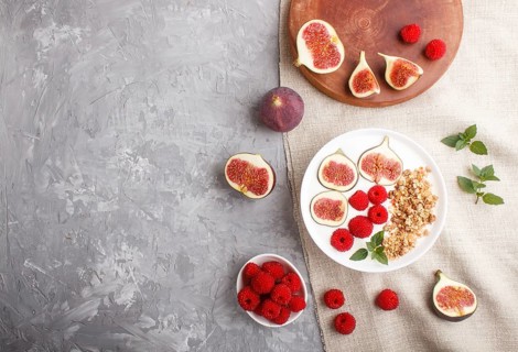 Yoghurt with raspberry, granola and figs in white plate on a gray concrete background and linen