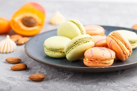 Orange and green macarons or macaroons cakes on blue ceramic plate on a gray concrete background.