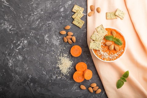 Carrot cream soup with sesame seeds, almonds and snacks in white bowl on a black concrete