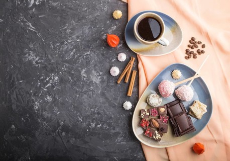 A pieces of homemade chocolate with coconut candies and a cup of coffee on a black concrete