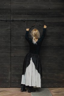 Full body shot of a young blonde caucasian woman reaching an antique lock of a wooden door above