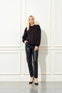 A stylish woman standing against a white, panelled wall. She is dressed in a dark, patterned