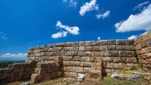 An ancient wall of stones under a blue sky with fluffy clouds, Ancient city wall, Archaeological