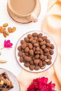 Almond in chocolate dragees on ceramic plate and a cup of coffee on white concrete background and