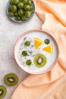 Yogurt with kiwi, gooseberry, chia in ceramic bowl on gray concrete background and orange linen