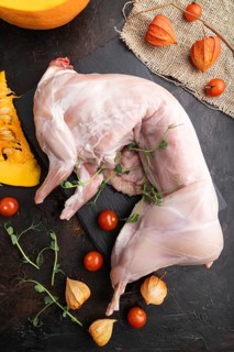 Whole raw rabbit with pumpkin, tomatoes, pea sprouts on a black concrete background and linen