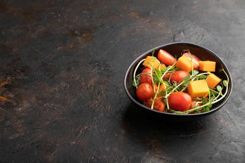 Vegetarian vegetable salad of tomatoes, pumpkin, microgreen pea sprouts on black concrete