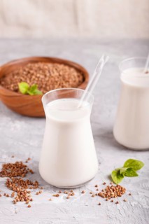 Organic non dairy buckwheat milk in glass and wooden plate with buckwheat seeds on a gray concrete