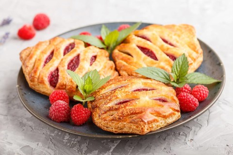 Puff pastry buns with strawberry jam on blue ceramic plate on gray concrete background, mint leaves