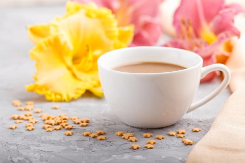 Yellow anf purple day-lilies cup of coffee on a gray concrete background, with orange textile.