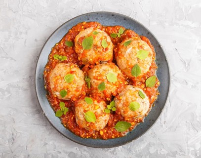 Pork meatballs with tomato sauce, oregano leaves, spices and herbs on blue ceramic plate on a gray