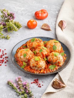 Pork meatballs with tomato sauce, oregano leaves, spices and herbs on blue ceramic plate on a gray