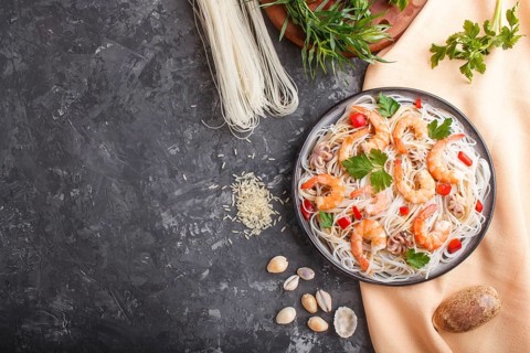 Rice noodles with shrimps or prawns and small octopuses on gray ceramic plate on a black concrete