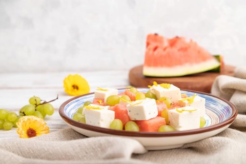 Vegetarian salad with watermelon, feta cheese, and grapes on blue ceramic plate on white wooden