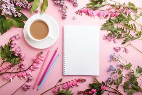 Purple lilac and bleeding heart flowers and a cup of coffee with notebook and colored pencils on