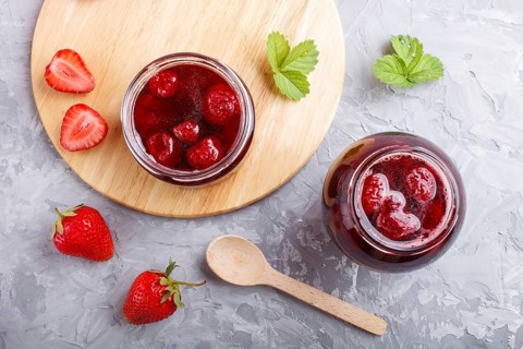 Strawberry jam in a glass jar with berries and leaves on gray concrete background. Homemade, top