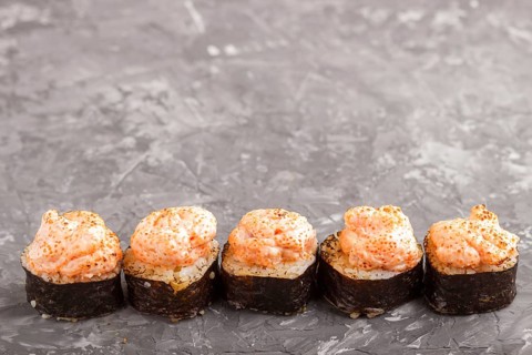 Japanese maki sushi rolls with flying fish roe, cheese on black concrete background. Side view,