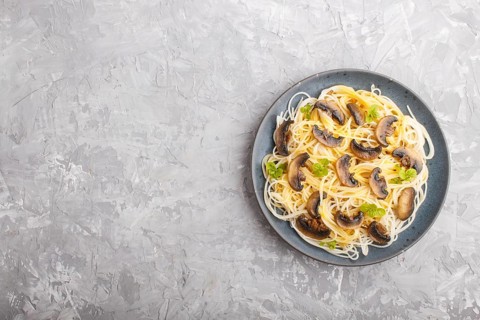 Rice noodles with champignons mushrooms, egg sauce and oregano on blue ceramic plate on a gray