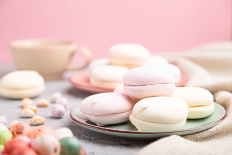 Colored zephyr or marshmallow with cup of coffee and dragees on a gray and pink background and