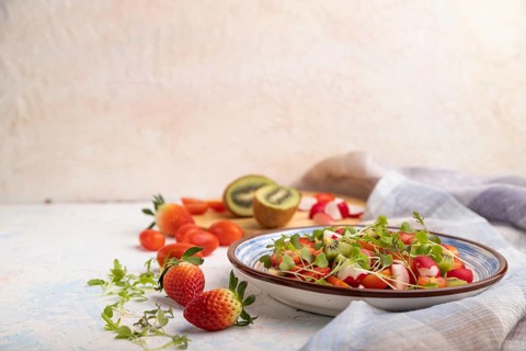 Vegetarian fruits and vegetables salad of strawberry, kiwi, tomatoes, microgreen sprouts on white
