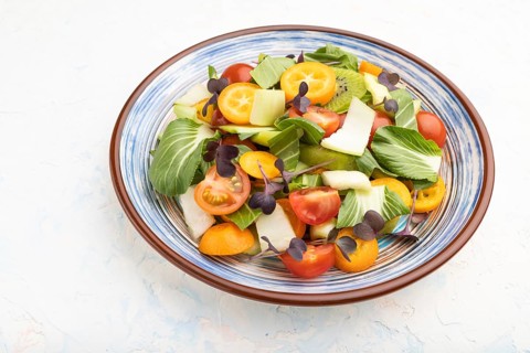 Vegetarian salad of pac choi cabbage, kiwi, tomatoes, kumquat, microgreen sprouts on a white