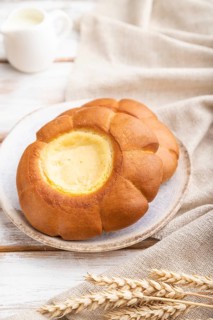 Sour cream bun with cup of coffee on a white wooden background and linen textile. Side view, close