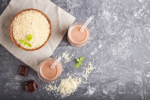 Organic non dairy rice chocolate milk in glass and wooden plate with rice seeds on a black concrete