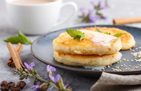 Cheese pancakes on a blue ceramic plate and a cup of coffee on a gray concrete background. side
