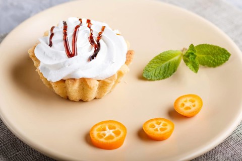 Cake with whipped egg cream on a light brown plate with kumquat slices and mint leaves on a gray