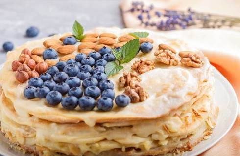 Homemade layered Napoleon cake with milk cream. Decorated with blueberry, almonds, walnuts,